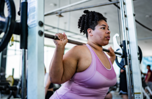 Mid adult woman doing squats with barbell at gym
