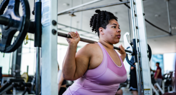 Mid adult woman doing squats with barbell at gym