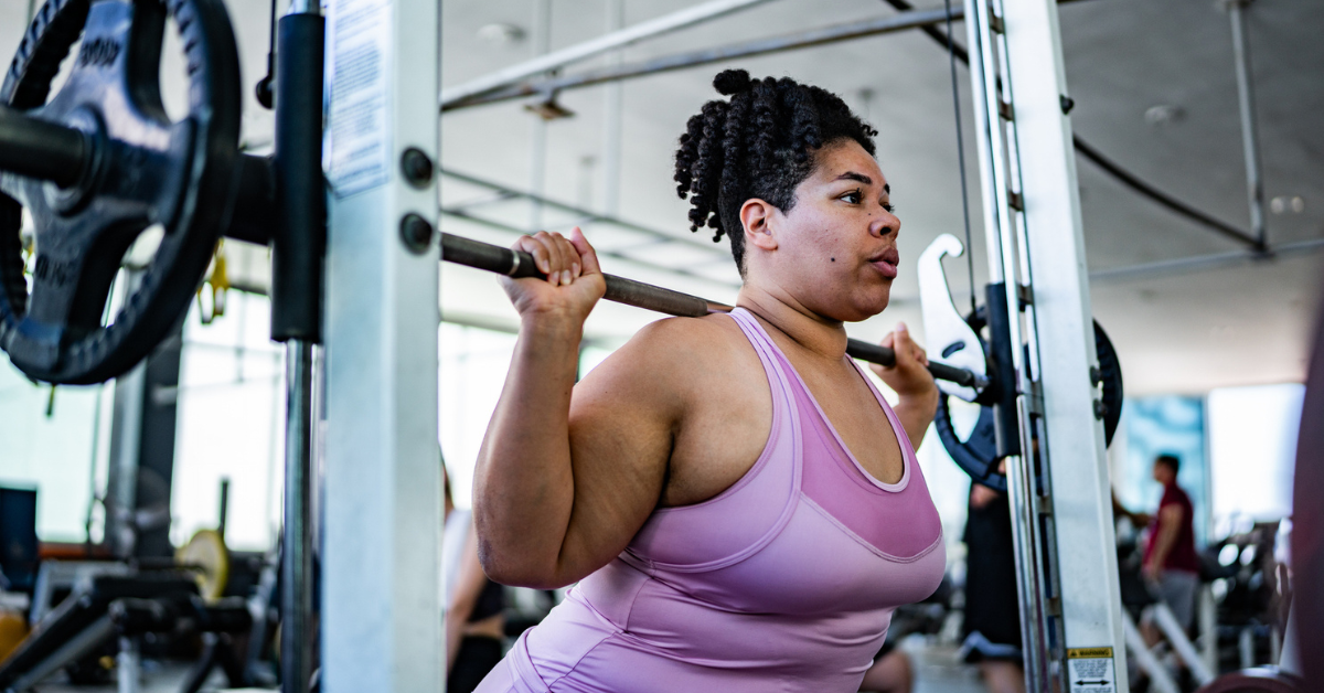 Mid adult woman doing squats with barbell at gym