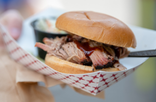 A person holds a pulled port slider sandwich with a side of coleslaw in a white and red paper basket.