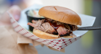 A person holds a pulled port slider sandwich with a side of coleslaw in a white and red paper basket.