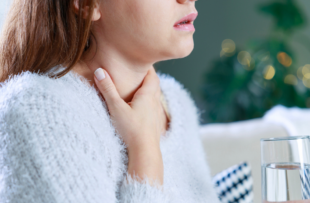 woman holding a glass of water touches her neck