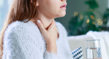 woman holding a glass of water touches her neck