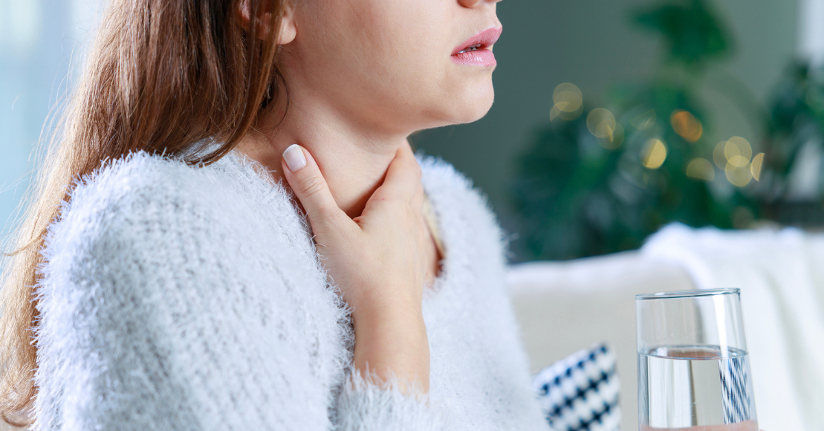 woman holding a glass of water touches her neck