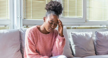 Portrait of a young girl sitting on the couch at home with a headache