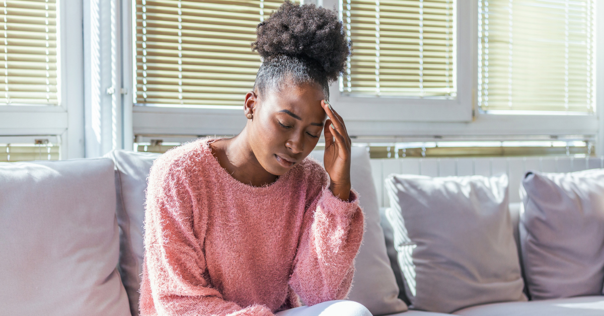 Portrait of a young girl sitting on the couch at home with a headache
