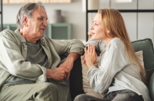 Father and daughter are talking on the couch in the living room.