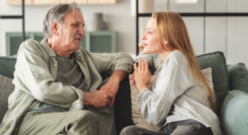Father and daughter are talking on the couch in the living room.