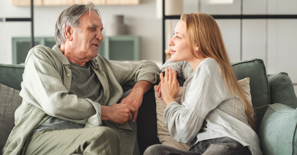 Father and daughter are talking on the couch in the living room.