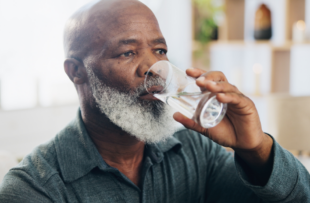 An older man in his living room drinking a glass of water.