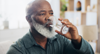 An older man in his living room drinking a glass of water.