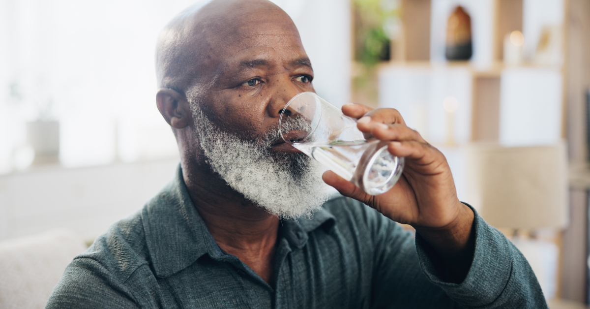An older man in his living room drinking a glass of water.