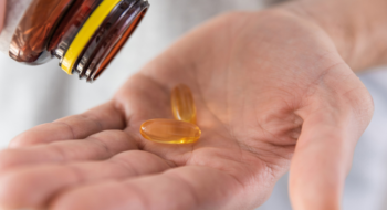 Man pouring fish oil capsules with omega 3, vitamin D in hand from medicine bottle. Nutritional supplement. Health support and treatment concept. Close up