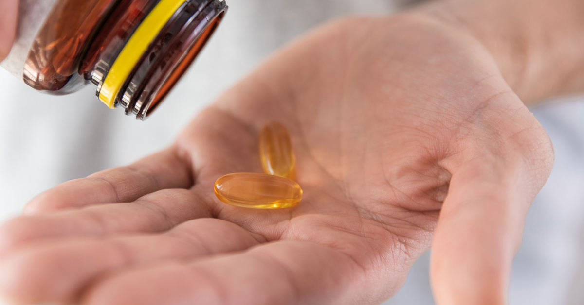 Man pouring fish oil capsules with omega 3, vitamin D in hand from medicine bottle. Nutritional supplement. Health support and treatment concept. Close up