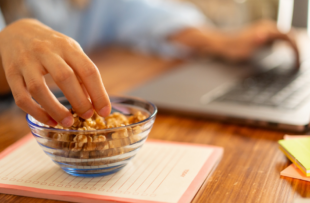 Healthy snack at work - hand reaching for nuts on desk, office setup, healthy eating habits, workplace nutrition, work-life balance.