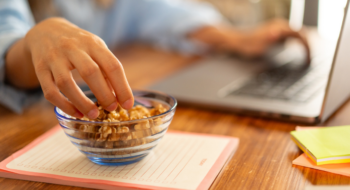 Healthy snack at work - hand reaching for nuts on desk, office setup, healthy eating habits, workplace nutrition, work-life balance.