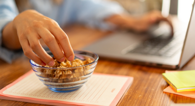 Healthy snack at work - hand reaching for nuts on desk, office setup, healthy eating habits, workplace nutrition, work-life balance.