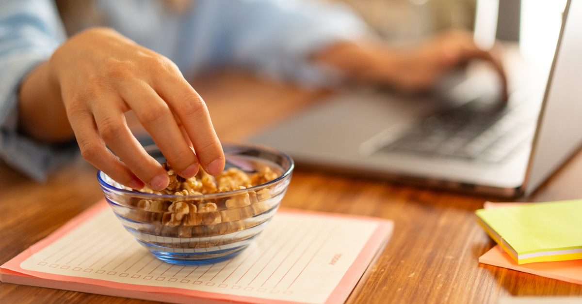 Healthy snack at work - hand reaching for nuts on desk, office setup, healthy eating habits, workplace nutrition, work-life balance.