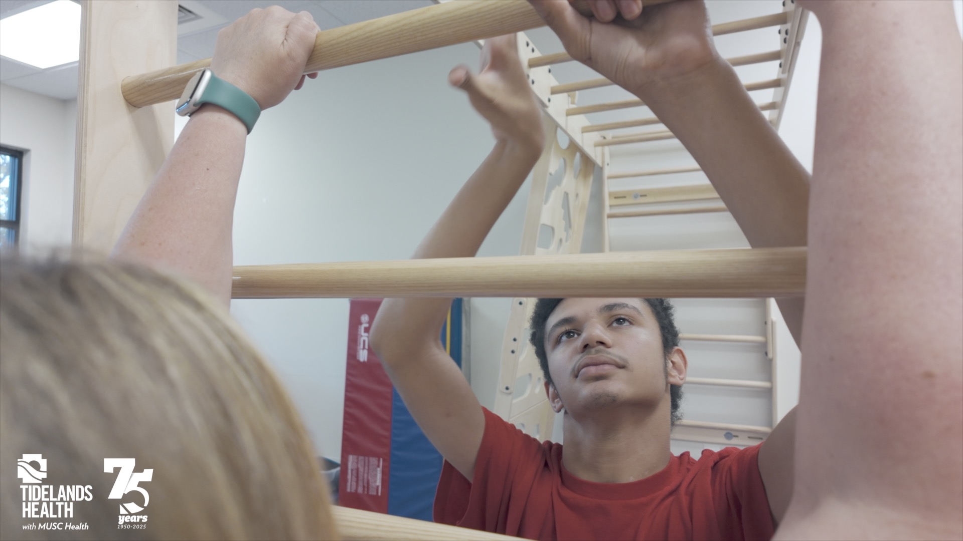 A young boy using the new therapy equipment that resembles monkey bars.