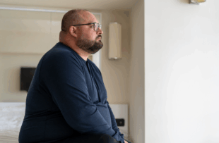man sitting on bed in hotel and looking out window
