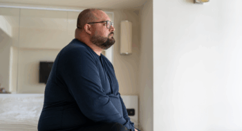 man sitting on bed in hotel and looking out window