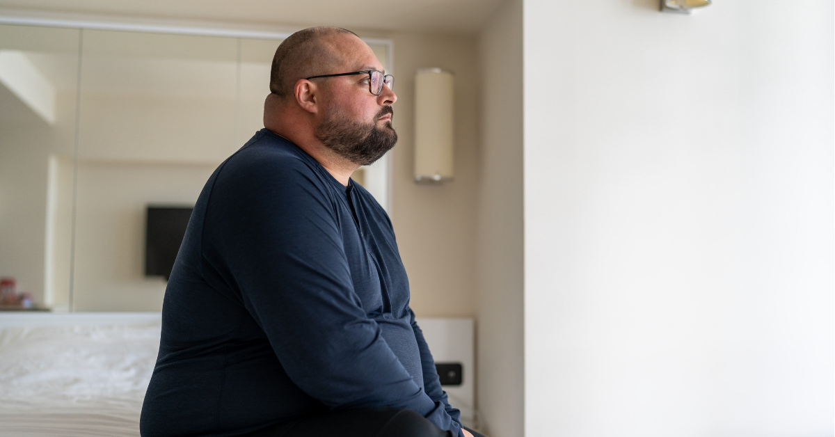 man sitting on bed in hotel and looking out window