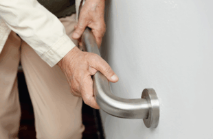 An elderly woman holding onto a handrail to keep herself steady.