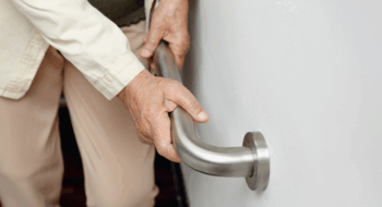 An elderly woman holding onto a handrail to keep herself steady.