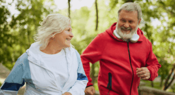 An older couple running through the woods and smiling.