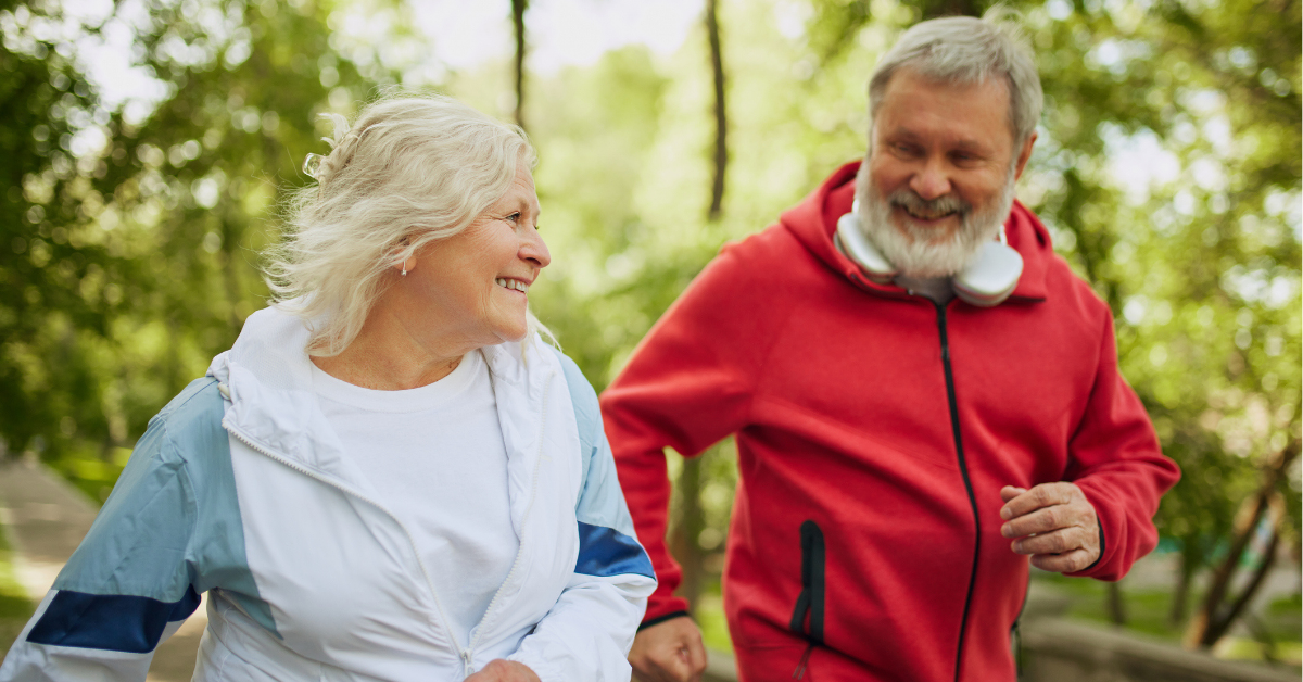 An older couple running through the woods and smiling.