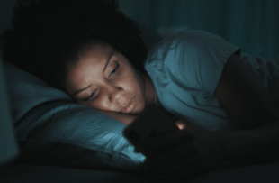 woman lying in bed at night, she can't sleep and she is checking her smartphone