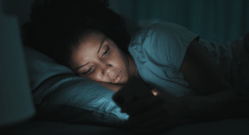 woman lying in bed at night, she can't sleep and she is checking her smartphone