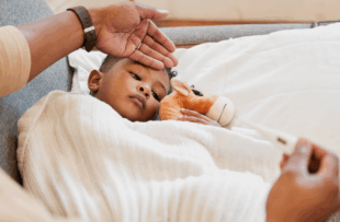 Parents hand on son's forehead for his temperature as she checks his fever with a thermometer.