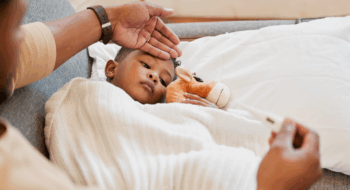Parents hand on son's forehead for his temperature as she checks his fever with a thermometer.