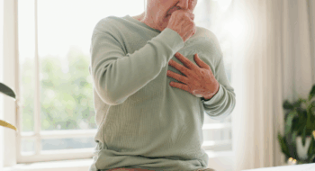 Coughing, sick and a person feeling chest for pain, heart attack or health problem at home.