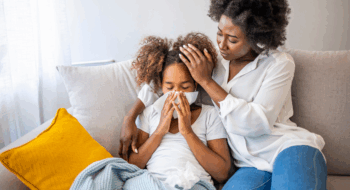Mother helping daughter blowing her nose on the sofa at home.