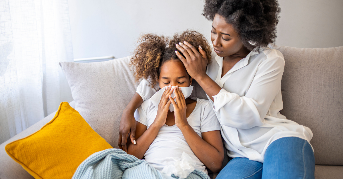 Mother helping daughter blowing her nose on the sofa at home.