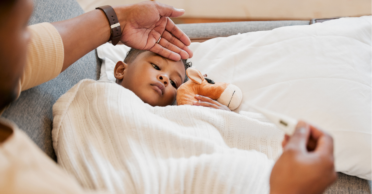 Parents hand on son's forehead for his temperature as she checks his fever with a thermometer.