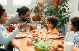 Happy parents and their kids talking while having breakfast together in dining room.