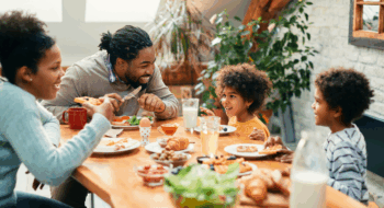 Happy parents and their kids talking while having breakfast together in dining room.