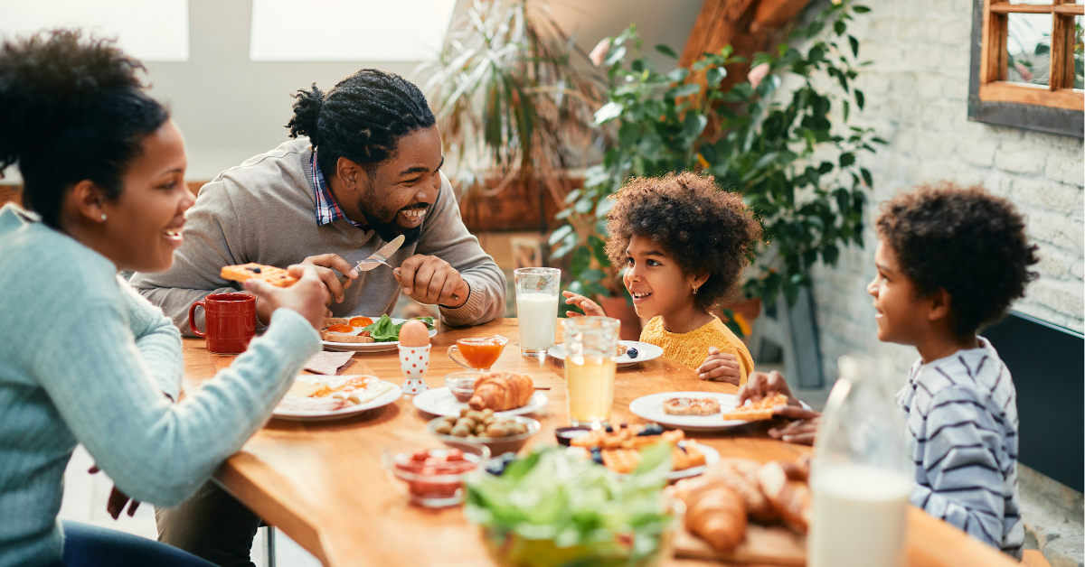 Happy parents and their kids talking while having breakfast together in dining room.