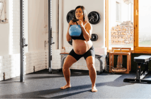 A pregnant woman is engaged in a kettlebell squat in a well-lit home gym.