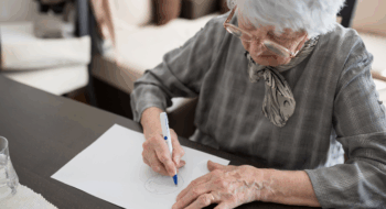 High angle view of a senior Caucasian woman doing Alzheimer's disease cognitive functions clock drawing self assessment test at home with positive results suggesting illness