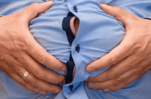 Abdominal bloating, big male belly held in hands, closeup