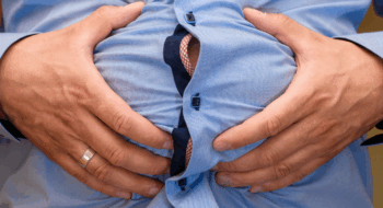 Abdominal bloating, big male belly held in hands, closeup