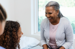 An unrecognizable female nurse takes notes as the senior adult woman and the female doctor laugh together.