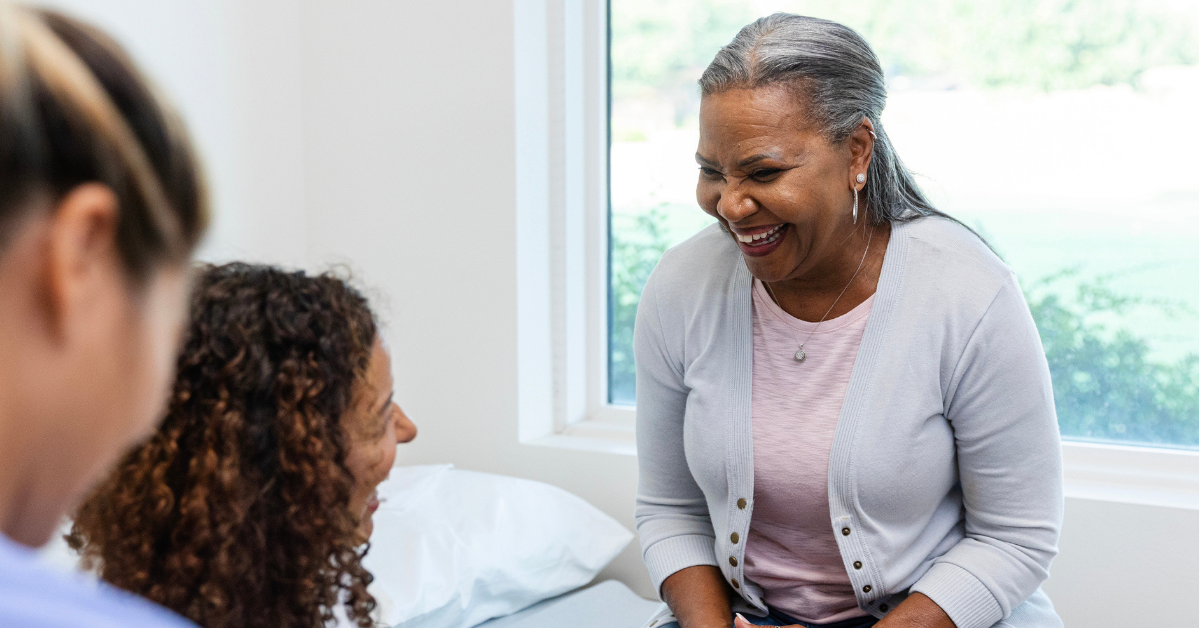 An unrecognizable female nurse takes notes as the senior adult woman and the female doctor laugh together.