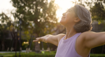 middle age mindful happy old woman open arm yoga deep calm stress relief outdoor nature public park sun light