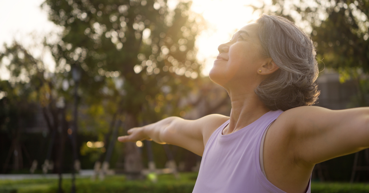 middle age mindful happy old woman open arm yoga deep calm stress relief outdoor nature public park sun light